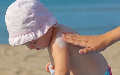 a mother applying sunscreen to her son on the beach